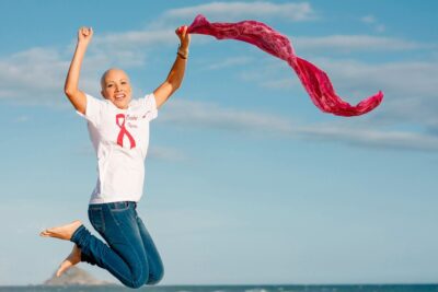 mulher-pulando-com-lenco-rosa-em-frente-a-fundo-azul-dia-mundial-do-combate-ao-cancer